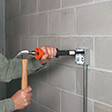 Workman uses hammer and Hammershot to attach electrical box to concrete block wall